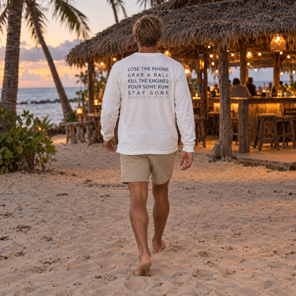 The white Bareboat Motto Long Sleeve worn, back view: Lose the phone. Grab a ball. Kill the engines. Pour some rum. Stay gone.