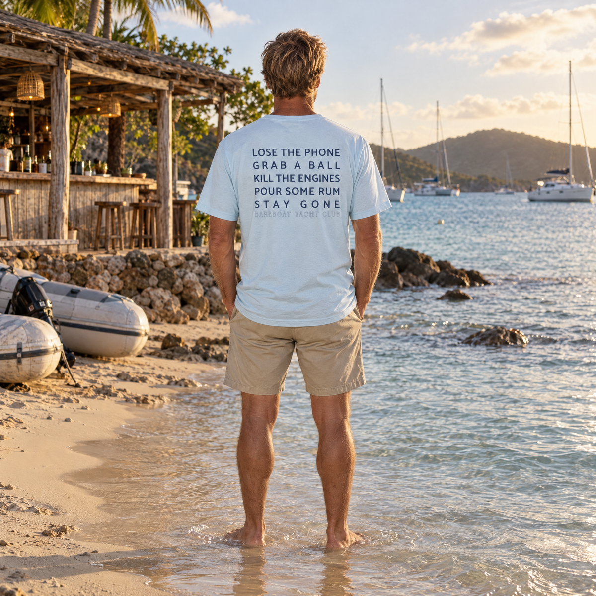 The chambray Bareboat Motto Tee worn, back view: Lose the phone. Grab a ball. Kill the engines. Pour some rum. Stay gone.