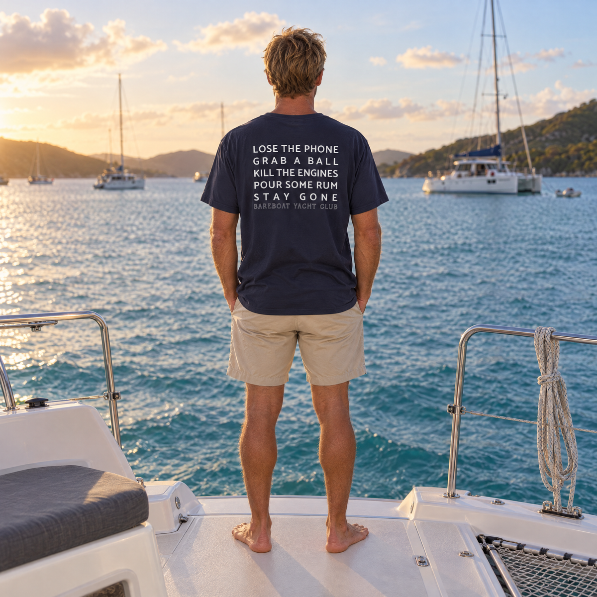 The navy Bareboat Motto Tee worn, back view: Lose the phone. Grab a ball. Kill the engines. Pour some rum. Stay gone.